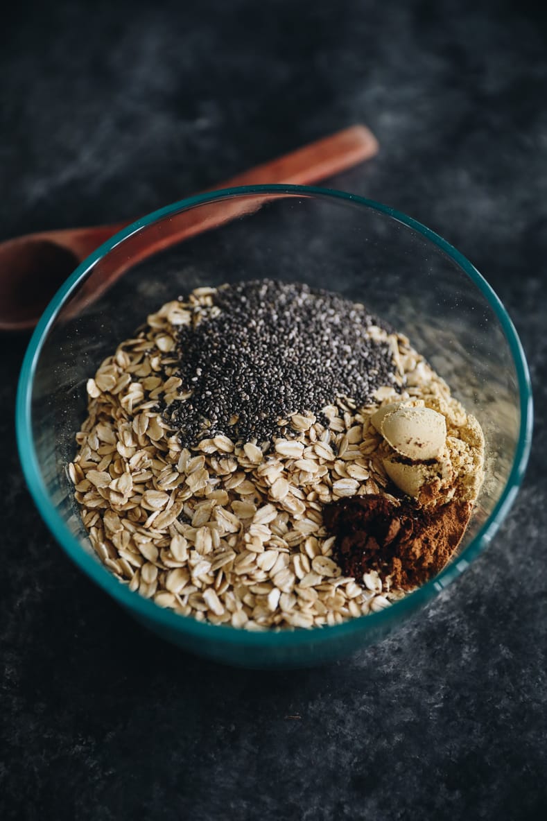 Dry ingredients of gingerbread overnight oats in a clear bowl. Wooden mixing spoon in the background.