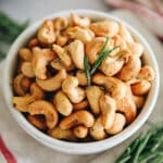 A white bowl of roasted cashews with rosemary.