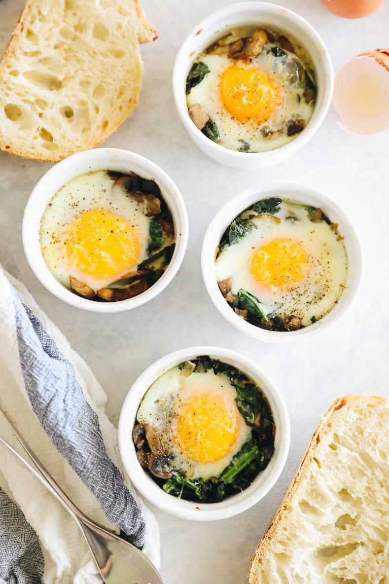 Overhead shot of four ramekins with vegetables and baked eggs. Sourdough bread slices surround the ramekins.