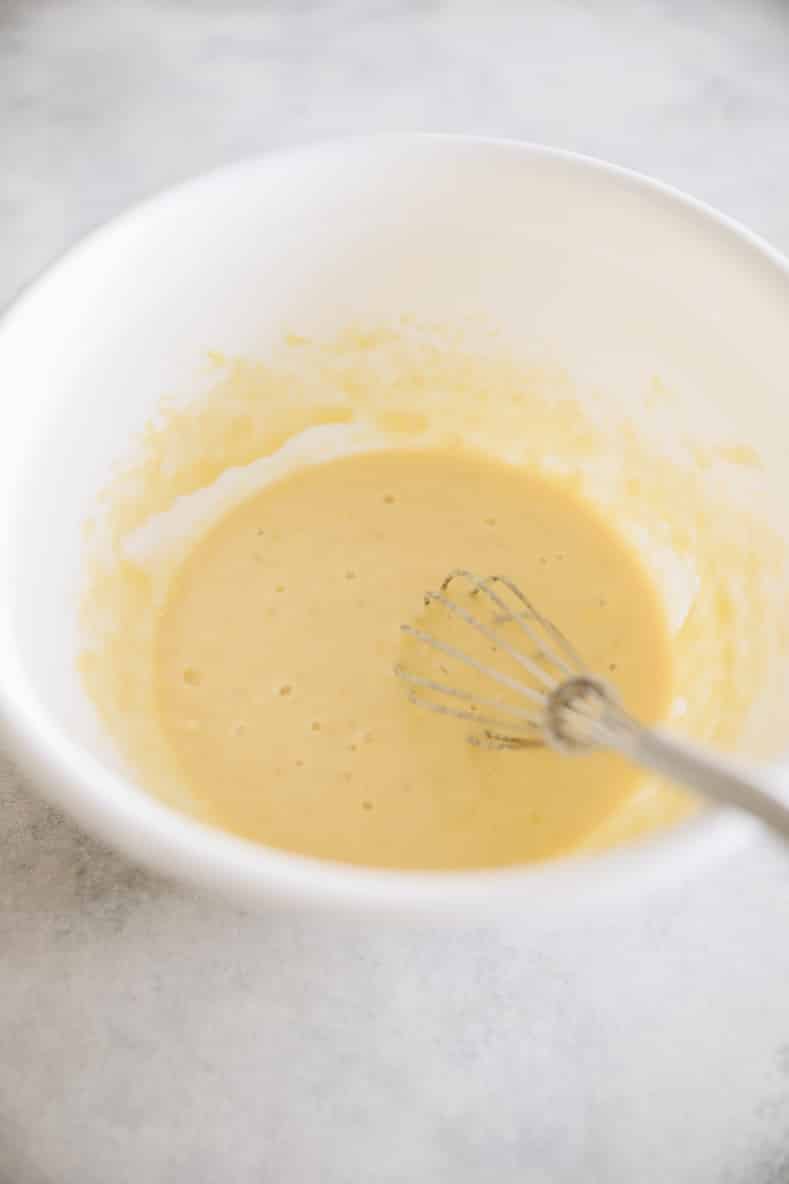 Banana protein pancake batter in a white mixing bowl with a whisk sitting in bowl.