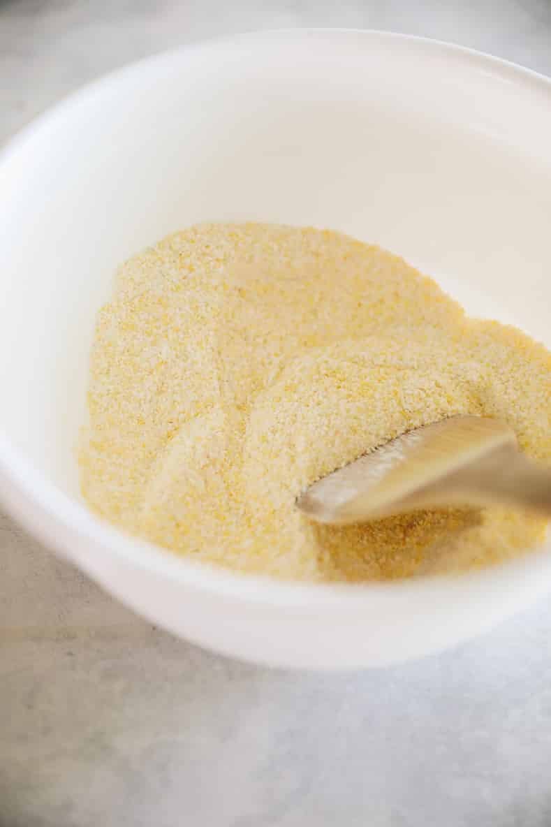 Dry ingredients for corn pancakes in a white mixing bowl with wooden spoon.