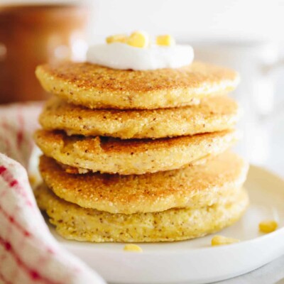 Corn pancakes stacked on a white plate and topped with a dollop of greek yogurt.