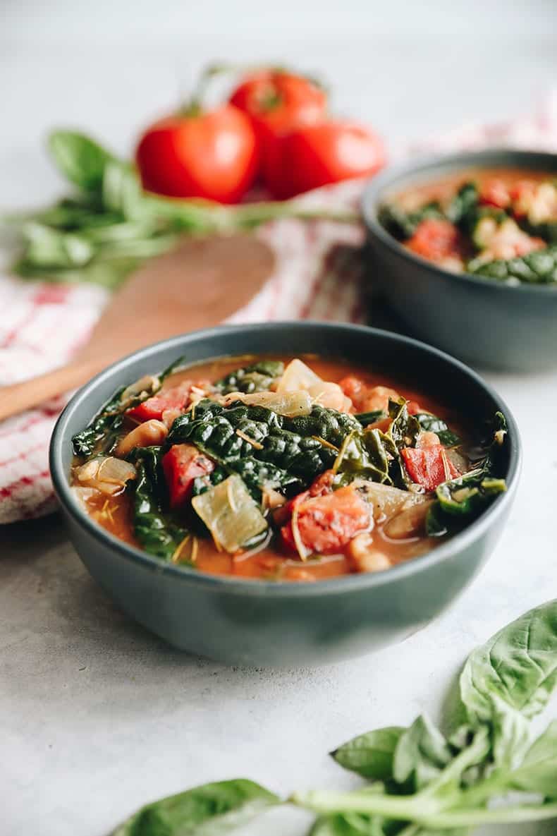 Bowl of soup with veggies and broth. Towel, wooden spoon and soup ingredients in the background.