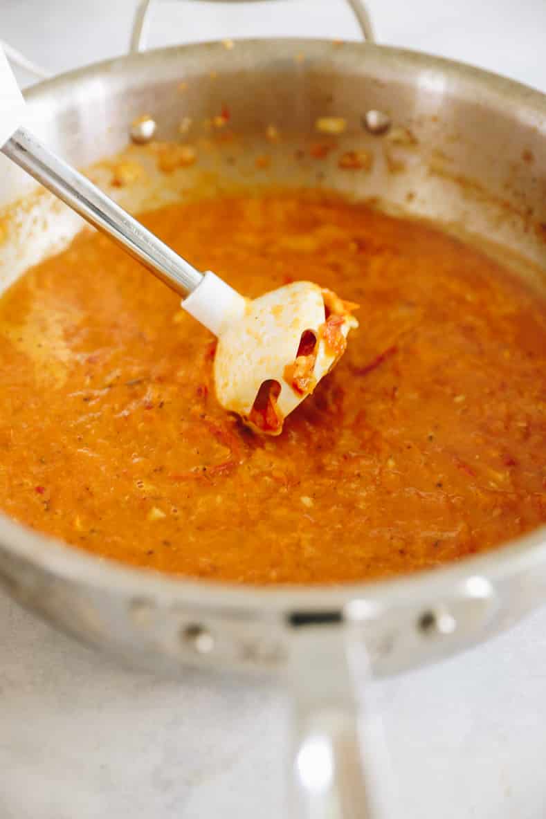 Una batidora de mano que mezcla la salsa arrabbiata picante en una cacerola grande.