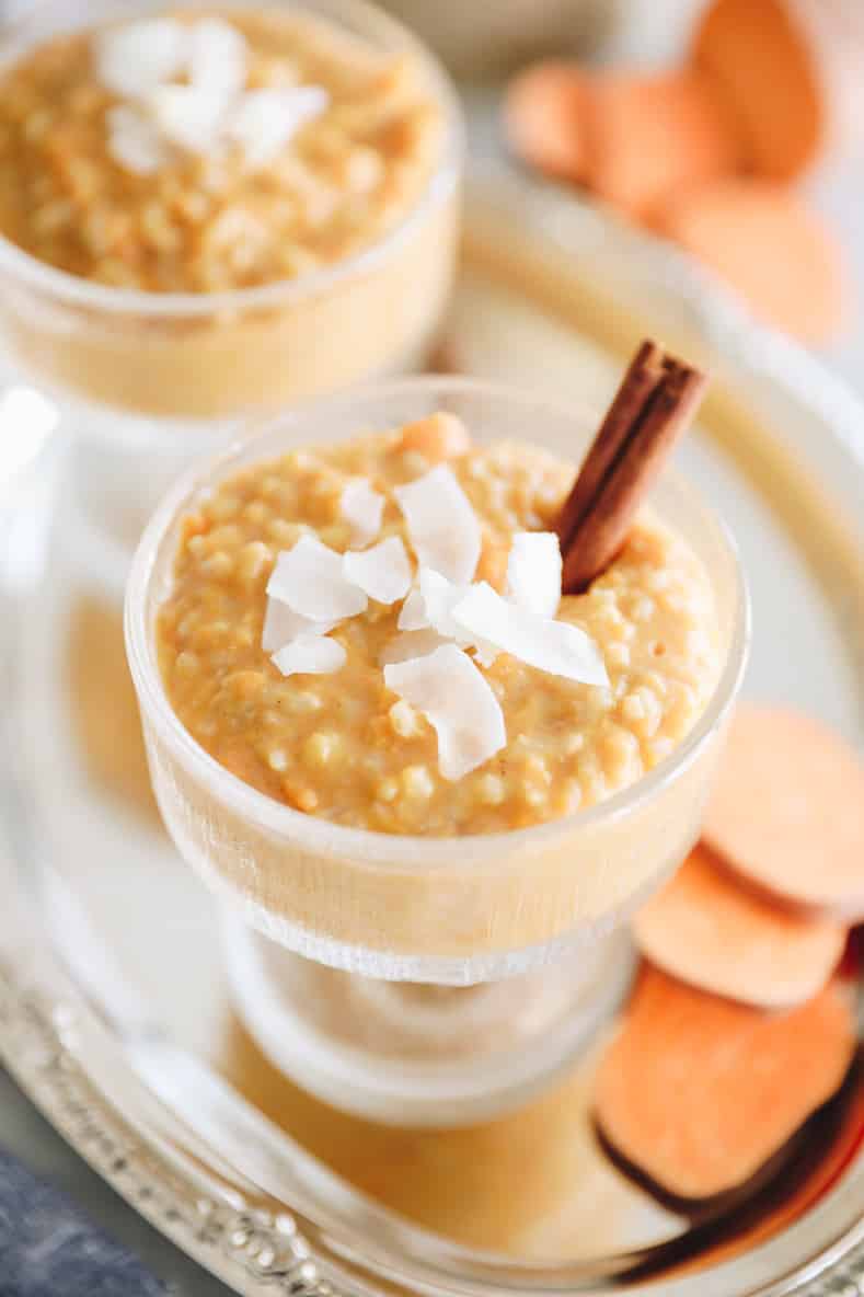 Sweet potato rice pudding in a clear serving dish with shredded coconut and a cinnamon stick on top.