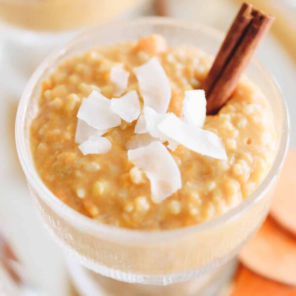 Sweet potato rice pudding in a clear serving dish with shredded coconut and a cinnamon stick on top.