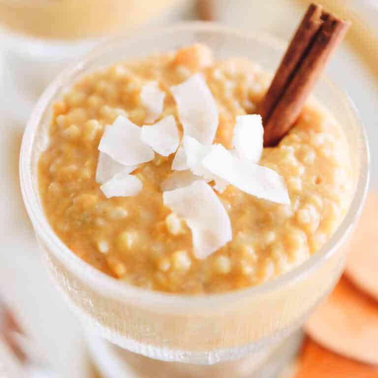 Sweet potato rice pudding in a clear serving dish with shredded coconut and a cinnamon stick on top.
