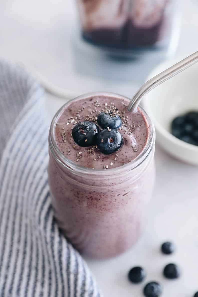 blueberry smoothie in a mason jar topped with blueberries and a straw