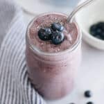 Blueberry smoothie in a mason jar with blueberries and a metal straw.