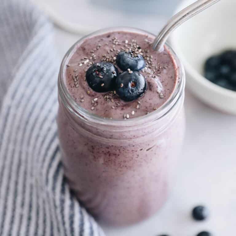 blueberry smoothie in a mason jar topped with blueberries and a metal straw.
