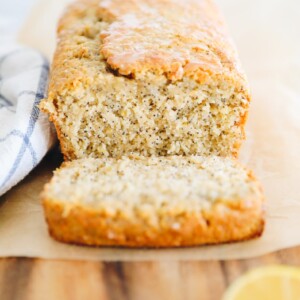 Loaf of lemon poppyseed bread on a wood cutting board. One slice cut off and laying in the front.