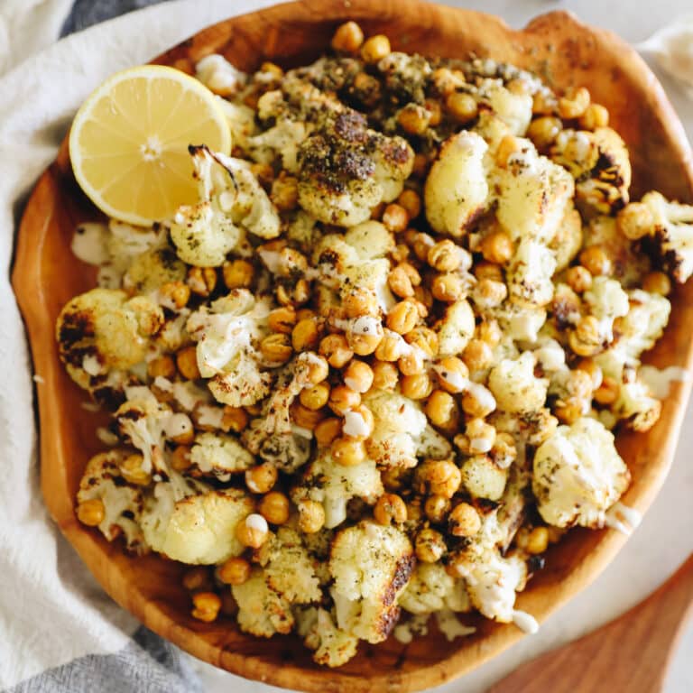 An overhead shot of a wooden serving bowl filled with roasted cauliflower and chickpeas.