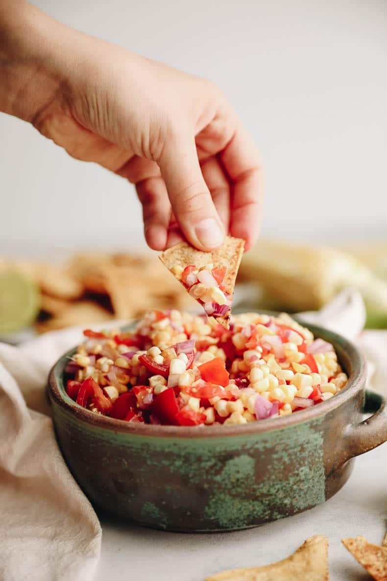 Get the best of summer with this fresh corn salsa paired with crispy baked chili lime tortilla chips. Homemade tortilla chips are so easy to make and the recipe is made extra simple without needing to cook the corn on the cob! #cornsalsa #vegan