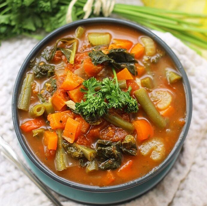 overhead image of vegetable soup recipe topped with parsley in a blue bowl.