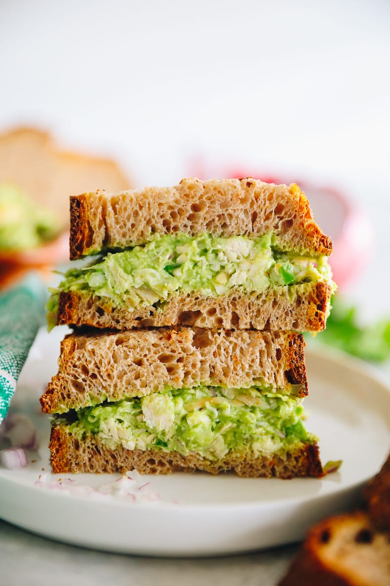 Close up shot of guacamole chicken salad sandwich on thick slices of wheat bread. Two halves of the sandwich are stacked on top of each other with the middle facing the camera.