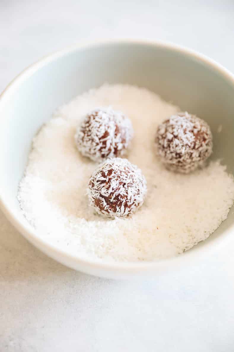 Almond joy energy balls sitting in a bowl of shredded coconut.