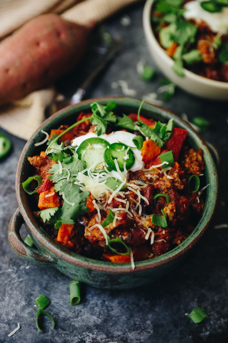 Turkey sweet potato chili in a bowl topped with cheese, yogurt, jalapenos and cilantro