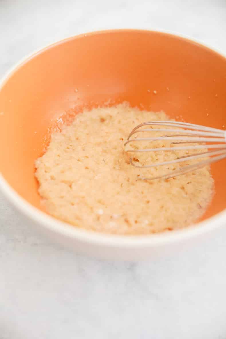 Orange bowl with doughy mixture and whisk inside.