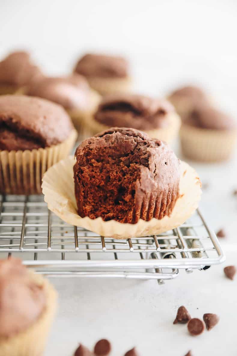 Chocolate gingerbread muffins on a wire rack. One muffin has it's liner peeled down with a bite taken out of it.