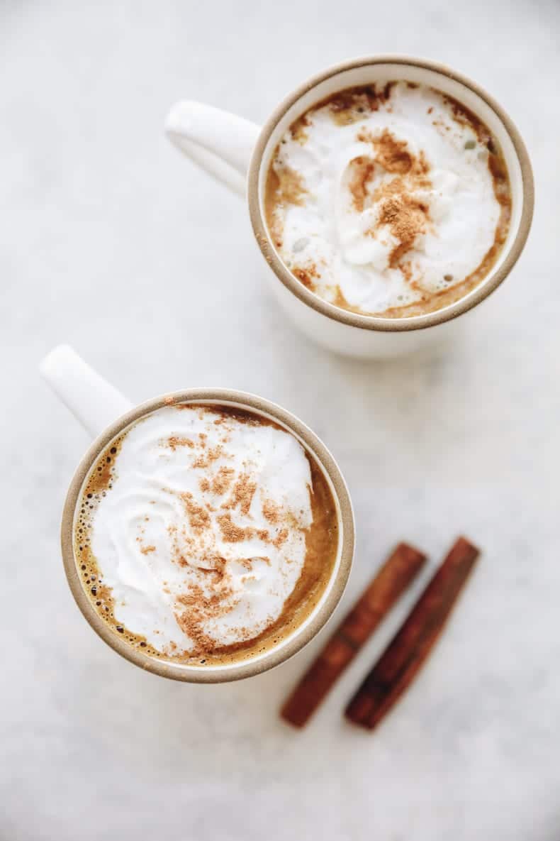 Overhead image of hot chocolate with whipped cream and cinnamon in white mugs
