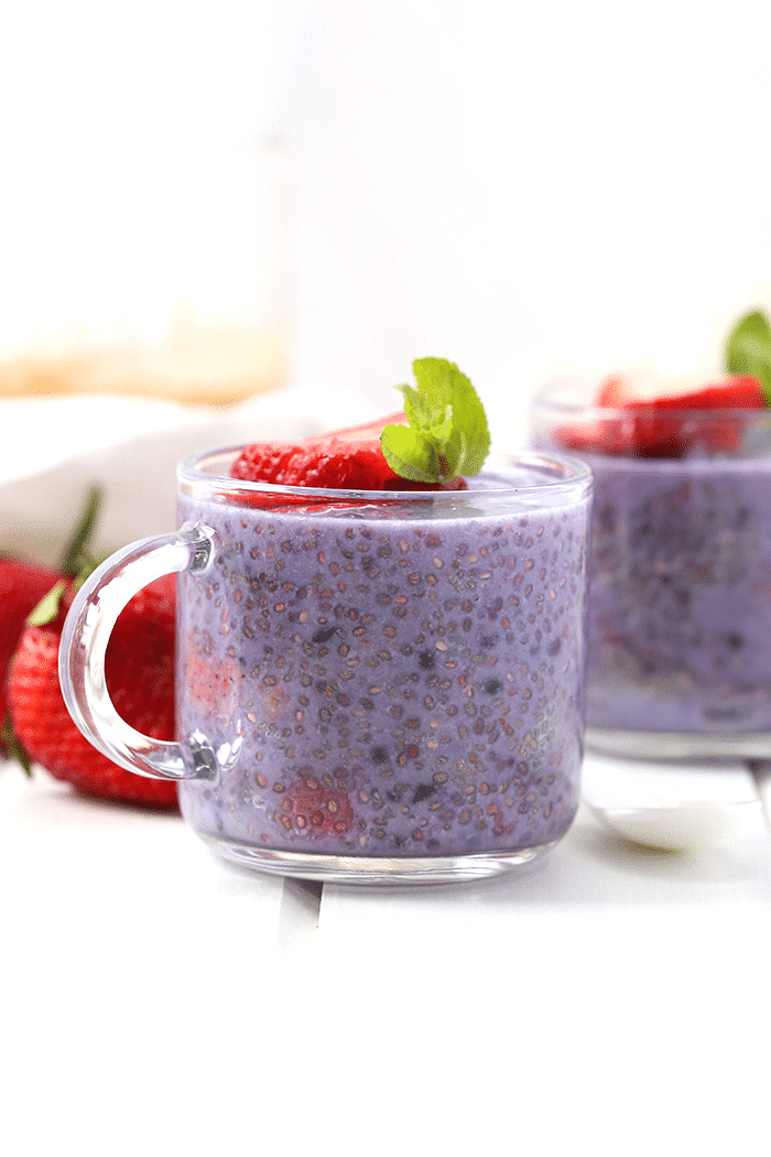 Glass mug filled with berry chia pudding. A sliced strawberry tops the chia pudding.