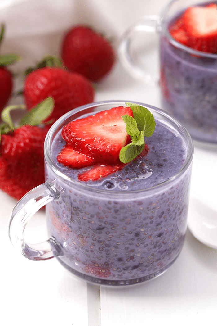 Glass mug of berry chia pudding topped with sliced strawberries. Full strawberries in the background.