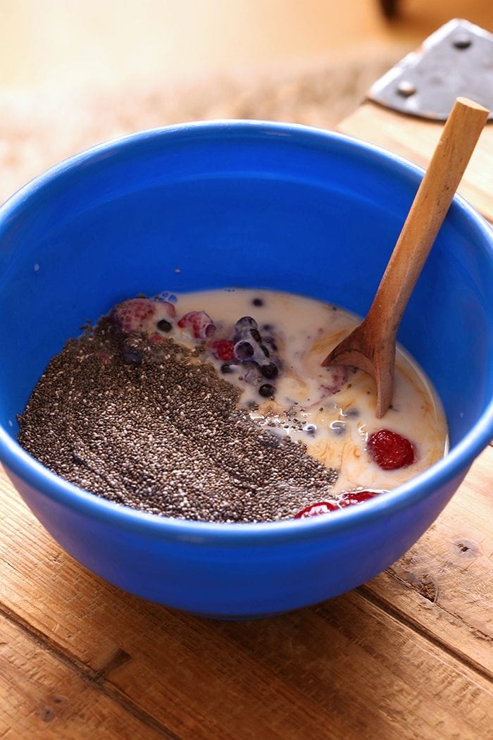 Blue mixing bowl with berry chia pudding ingredients and a wooden spoon.