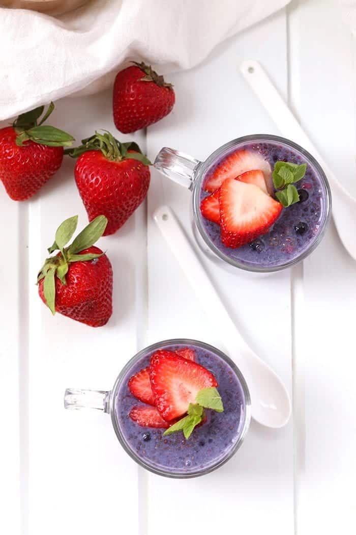 Overhead shot of two glass mugs filled with berry chia pudding. Strawberries and spoons surround the mugs.