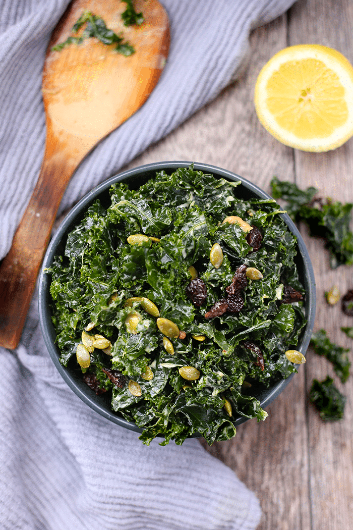 overhead image of a kale tahini salad with pumpkin seeds and cranberries in a blue bowl.