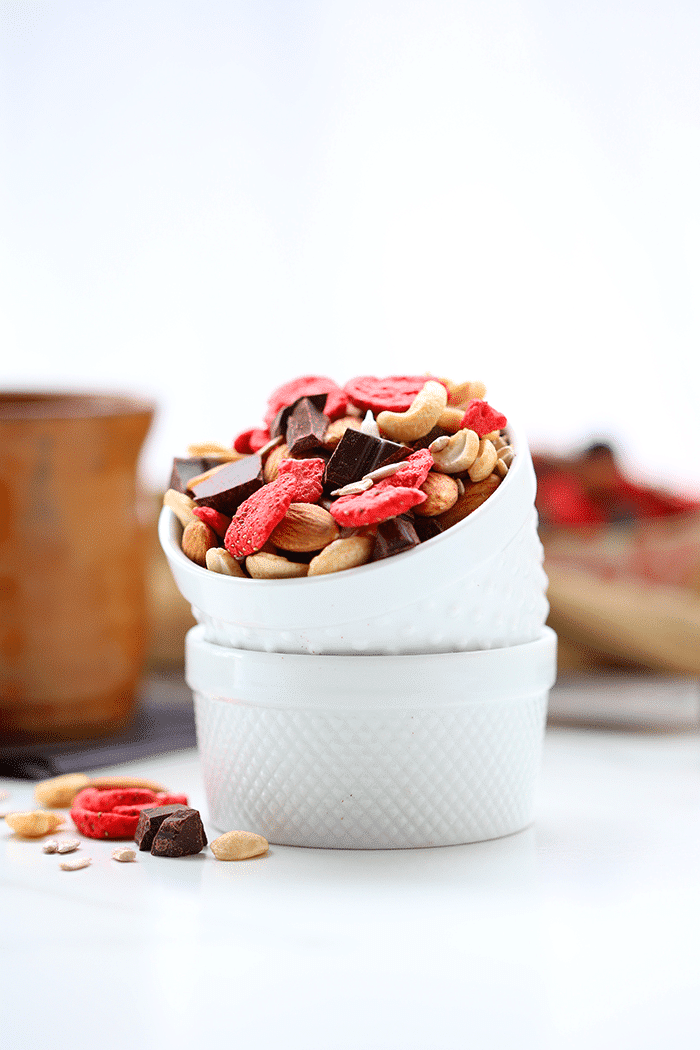 Two small bowls stacked and filled with trail mix made of mixed nuts, seeds, freeze dried strawberries and chocolate chunks.