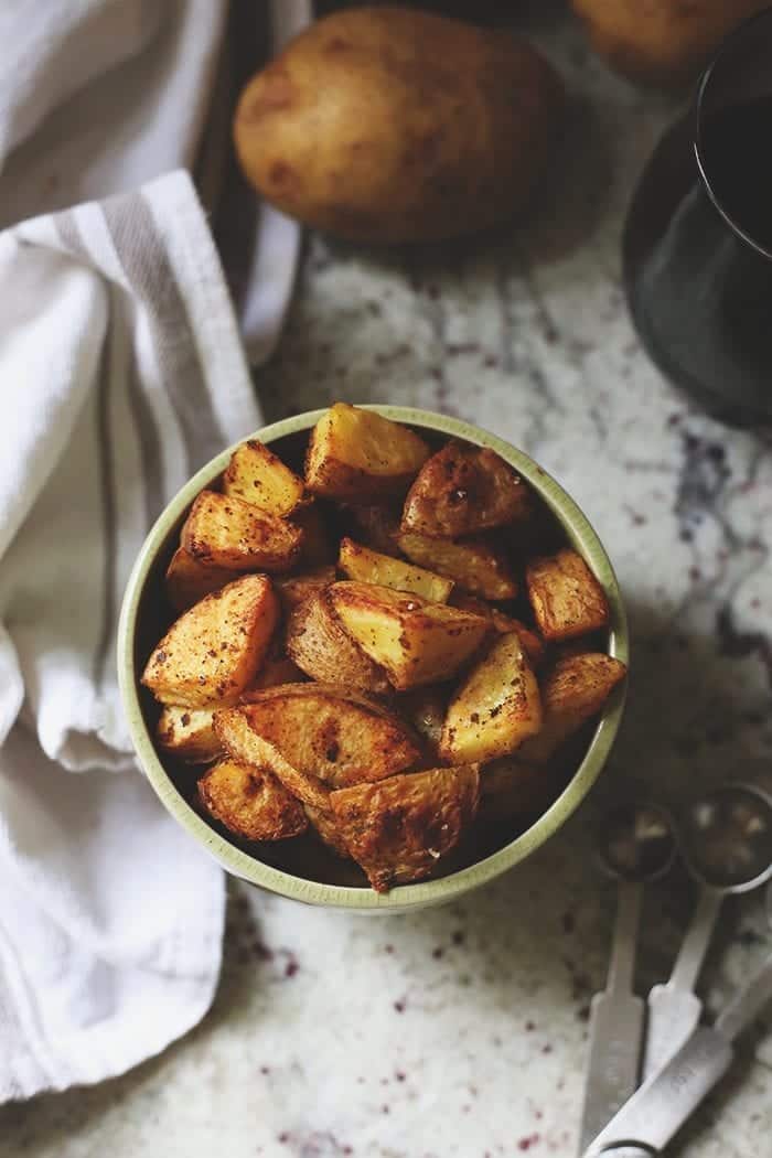 Overhead image of roasted potatoes in a green bowl topped with spices.