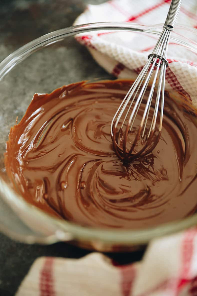 Melted chocolate in a clear mixing bowl with a whisk sitting on the edge of the bowl.