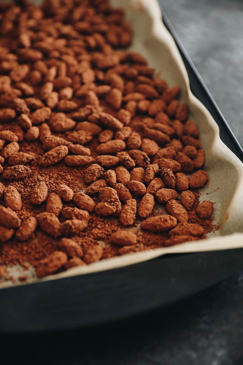Dark chocolate almonds spread on a baking sheet lined with parchment paper.