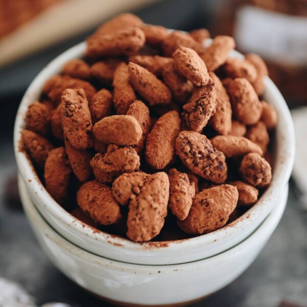 Close up shot of dark chocolate almonds in a white ceramic bowl.