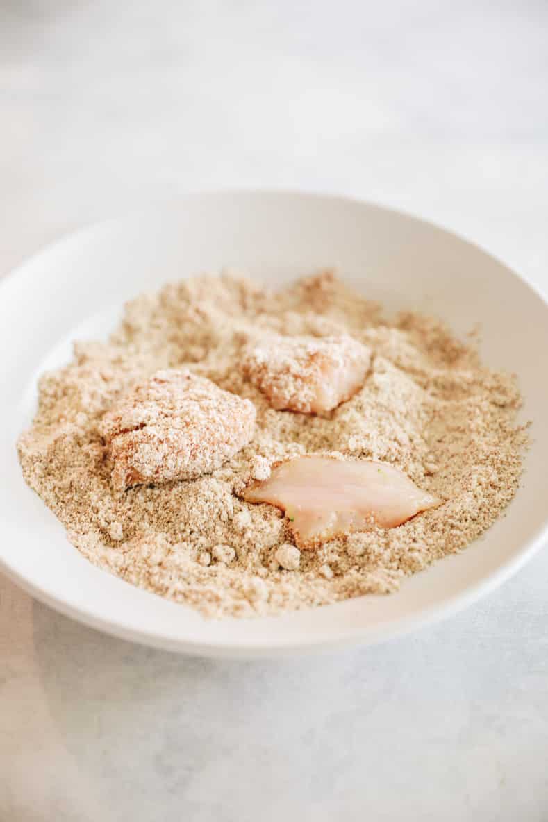 Pieces of raw chicken sitting in a bowl of spices for a coating before baking.