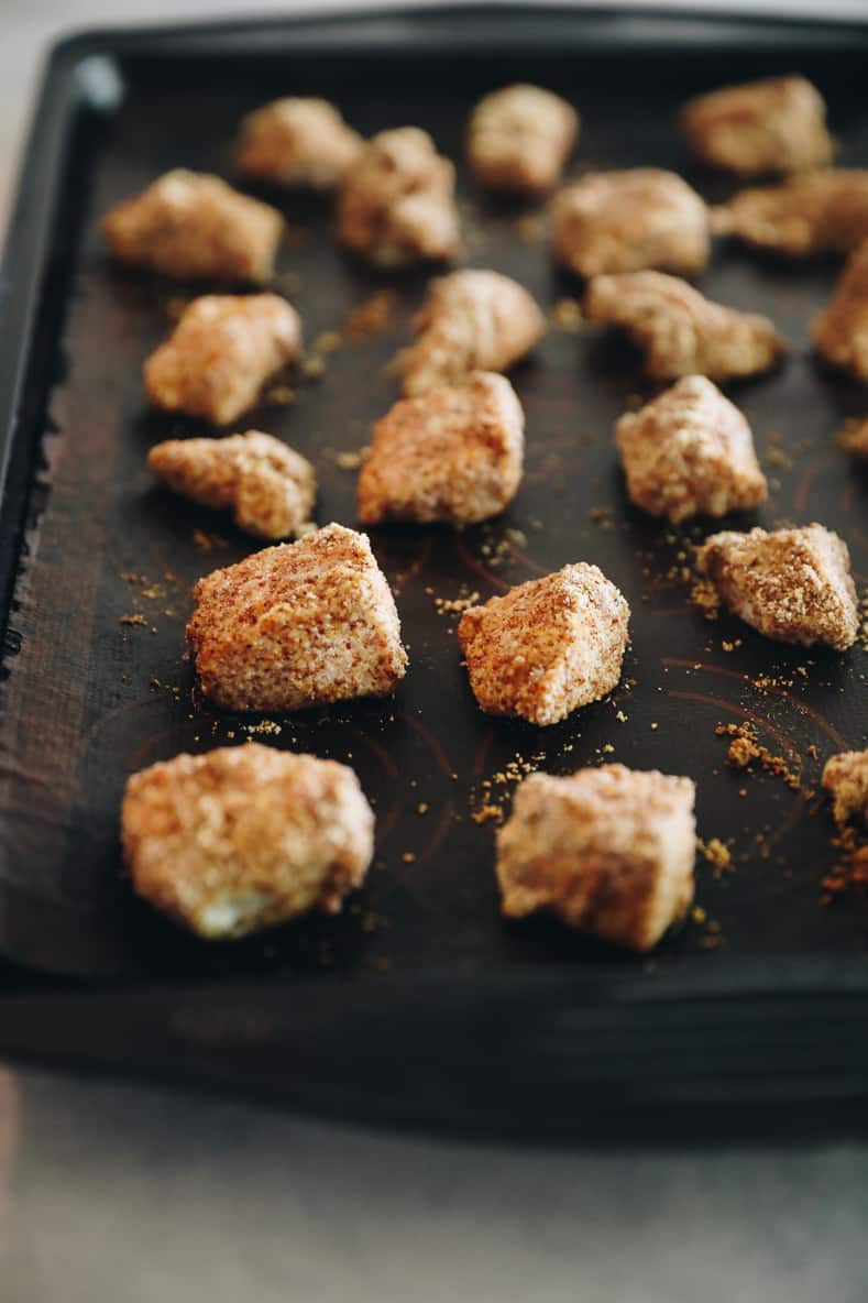Chicken bites covered in seasonings arranged on a baking sheet.