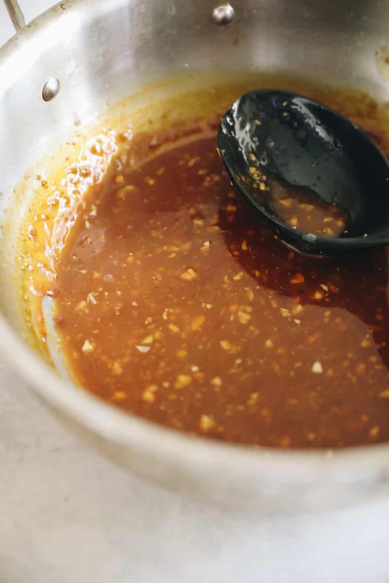 Sticky orange chicken sauce cooking in saucepan with black spoon sitting inside.