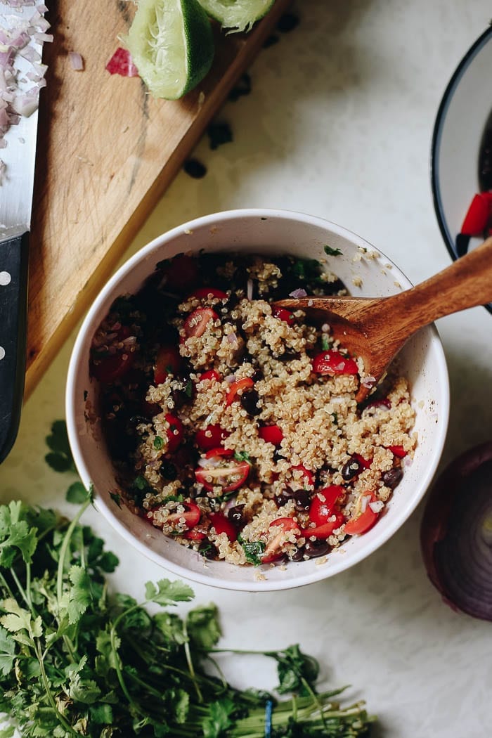 Overhead image of quinoa taco salad in a white mixing bowl with a wooden spoon sticking out. 