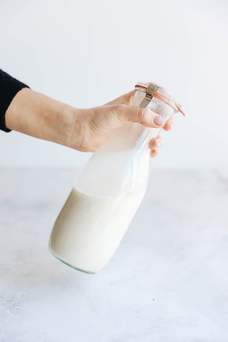 hand holding homemade oat milk in a glass jar