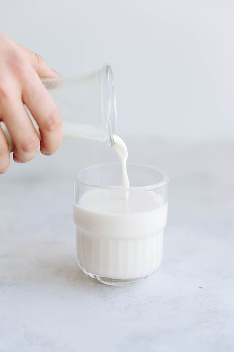 hand pouring homemade oat milk from a glass jar into a glass cup.