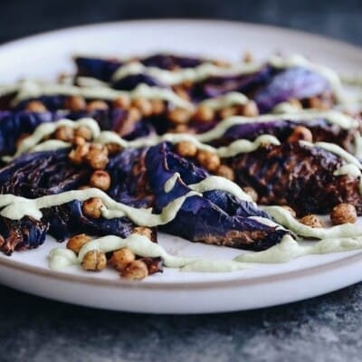 A horizontal picture of roasted cabbage steaks with crispy chickpeas and a cashew-based creamy herb sauce