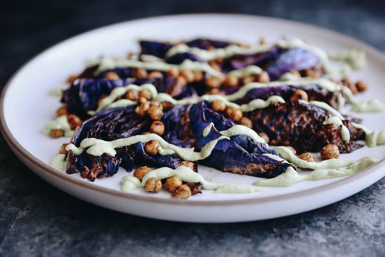 A horizontal picture of roasted cabbage steaks with crispy chickpeas and a cashew-based creamy herb sauce