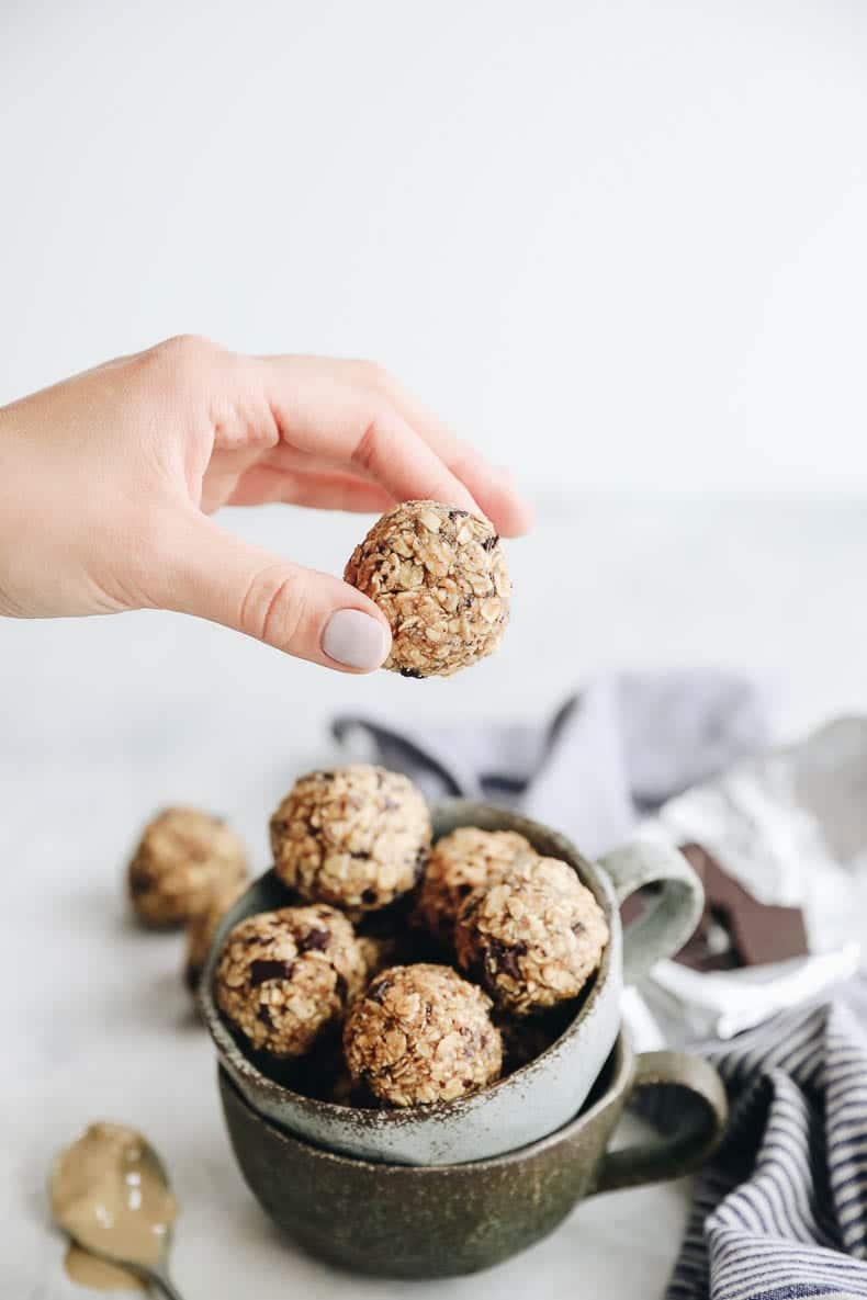 Two ceramic mugs stacked on top of each other and filled with tahini chocolate energy balls. One hand holding an energy ball over the mugs.