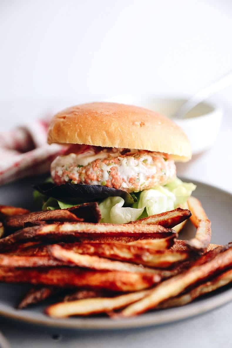 Salmon burgers in a bun with baked french fries.