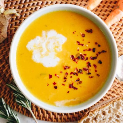 ginger carrot soup recipe in a white and blue bowl with coconut milk and red pepper flakes