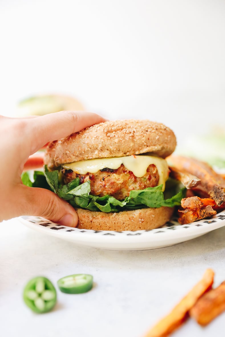 hand reaching for a jalapeno turkey burger in a bun with melted cheese.