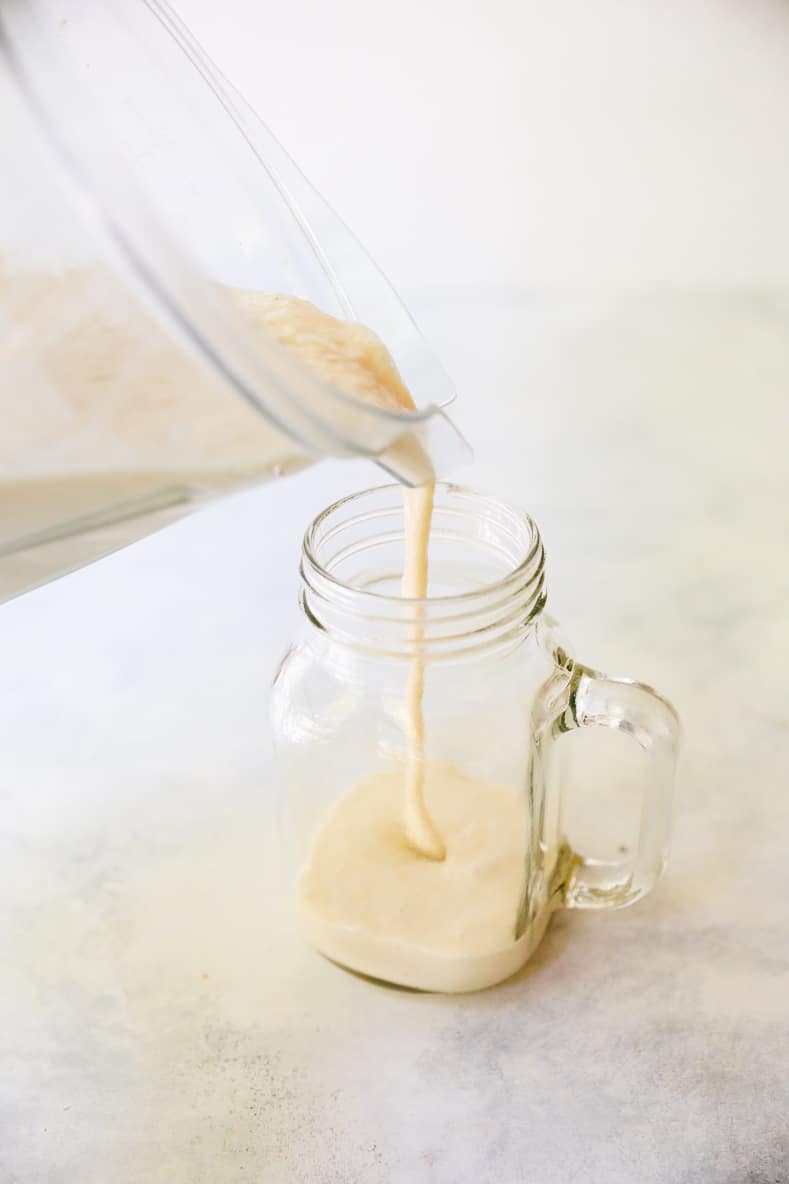 Pouring a banana peanut butter smoothie recipe from a blender into a mason jar