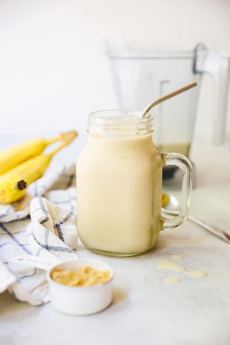 banana peanut butter smoothie in a mason jar with a straw and blender in the background.