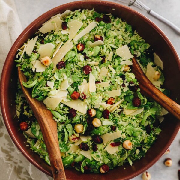 shredded brussel sprout salad in a brown bowl with serving spoons.