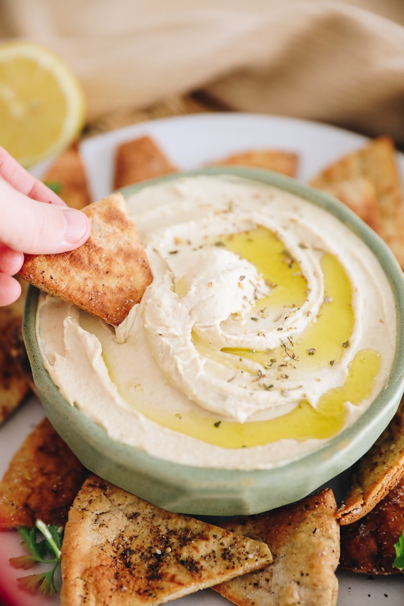 dipping a homemade pita chip into creamy hummus